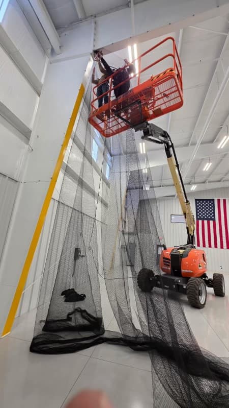 Bird netting barrier installation with technician on lift equipment
