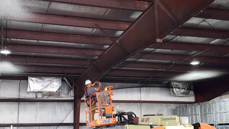 Technician on scissor lift installing bird netting on warehouse ceiling